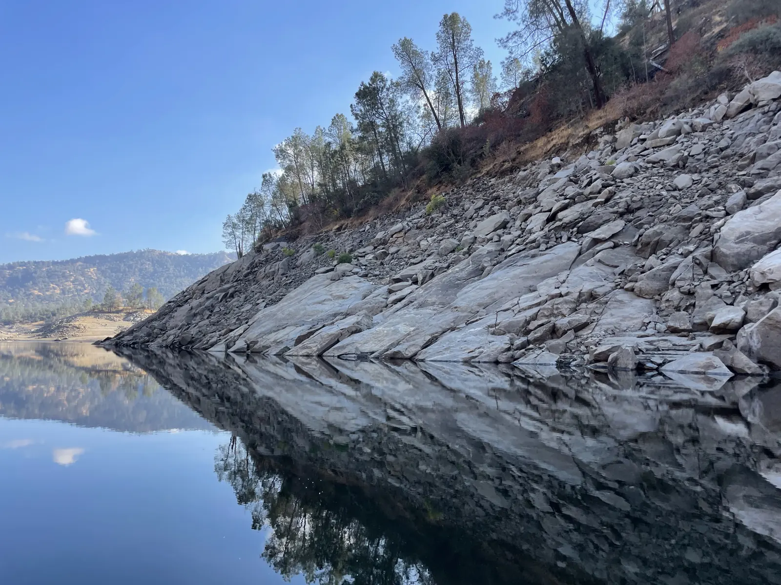 Pine-topped granite cliff mirrored in still lake water