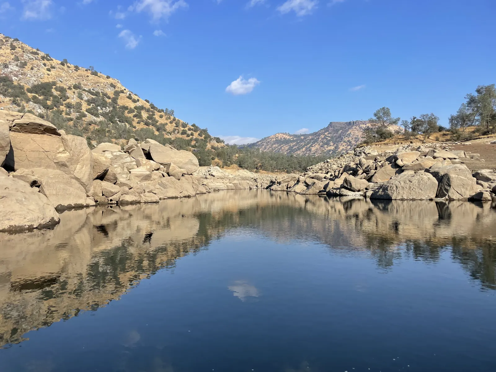 Granite boulders and oak hills reflected in calm Millerton Lake water