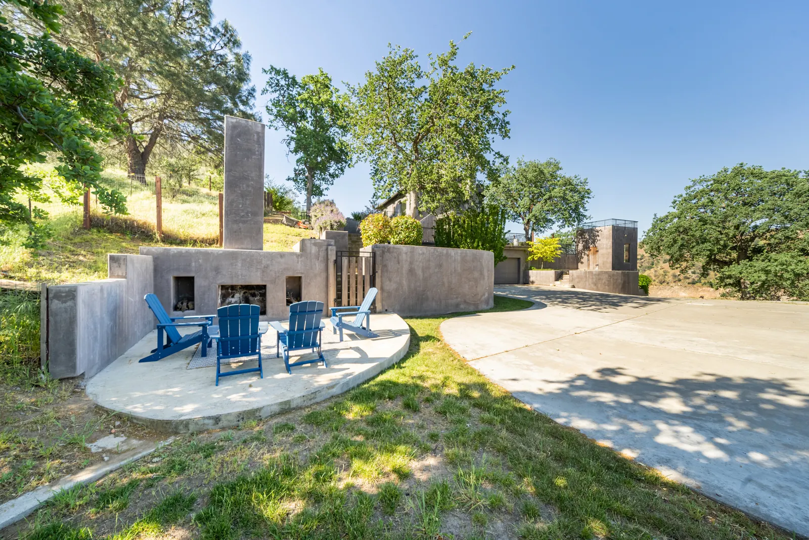 Outdoor fireplace with Adirondack chairs on a patio among oak trees
