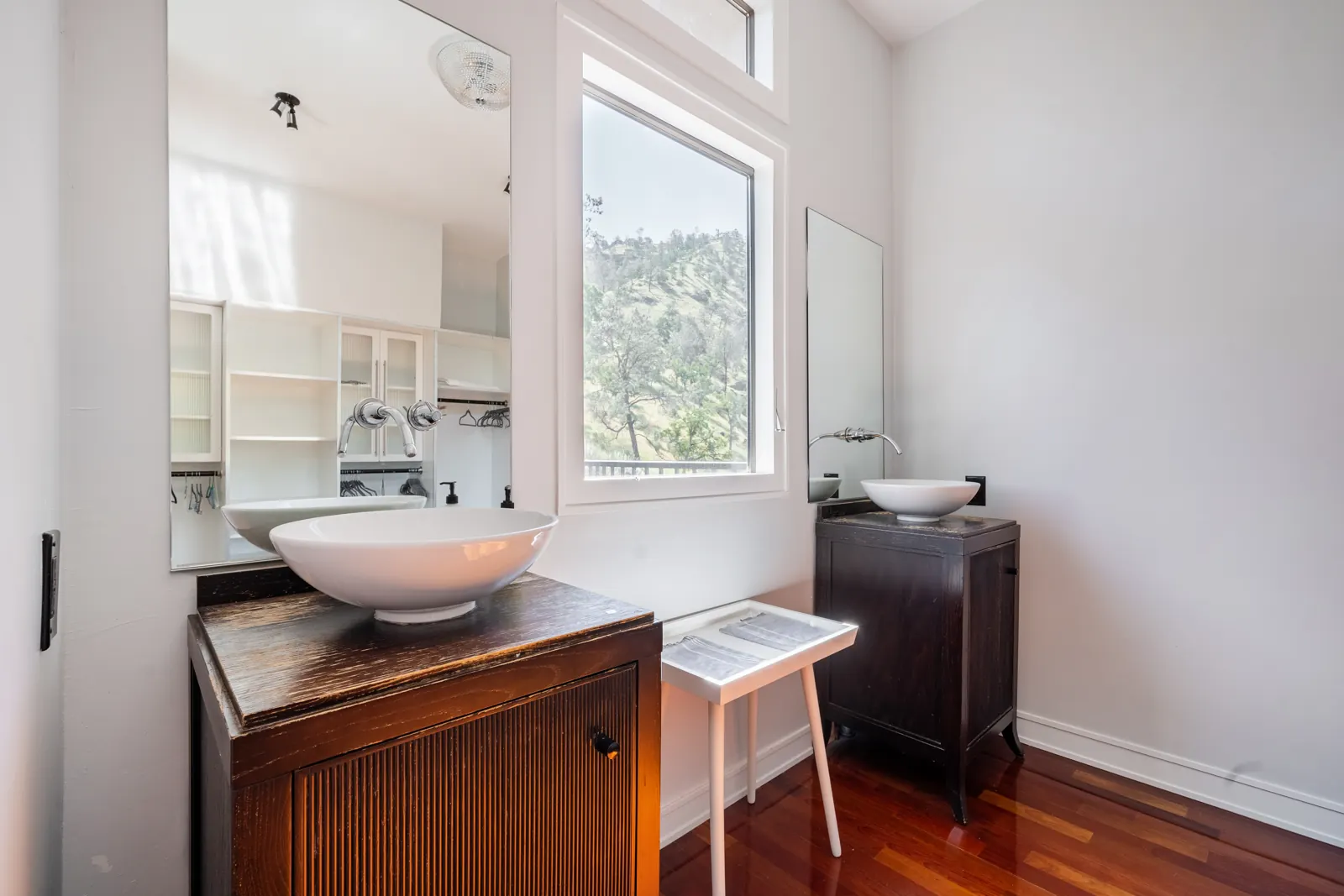 Two vessel sinks on wood vanities in the primary suite, with hill views through the window