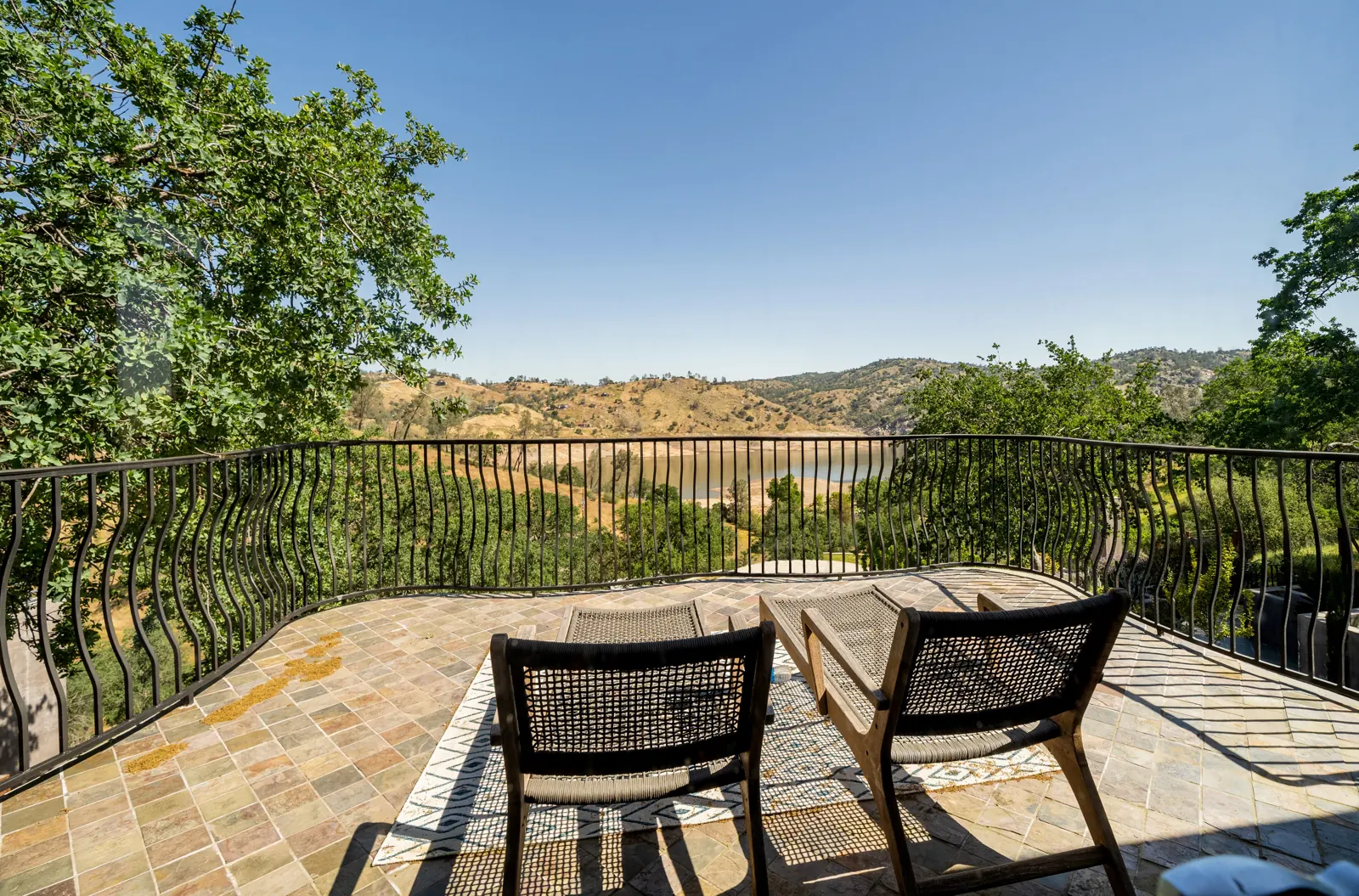 The primary suite's private balcony with two chairs, looking out over the oak hills and Millerton Lake