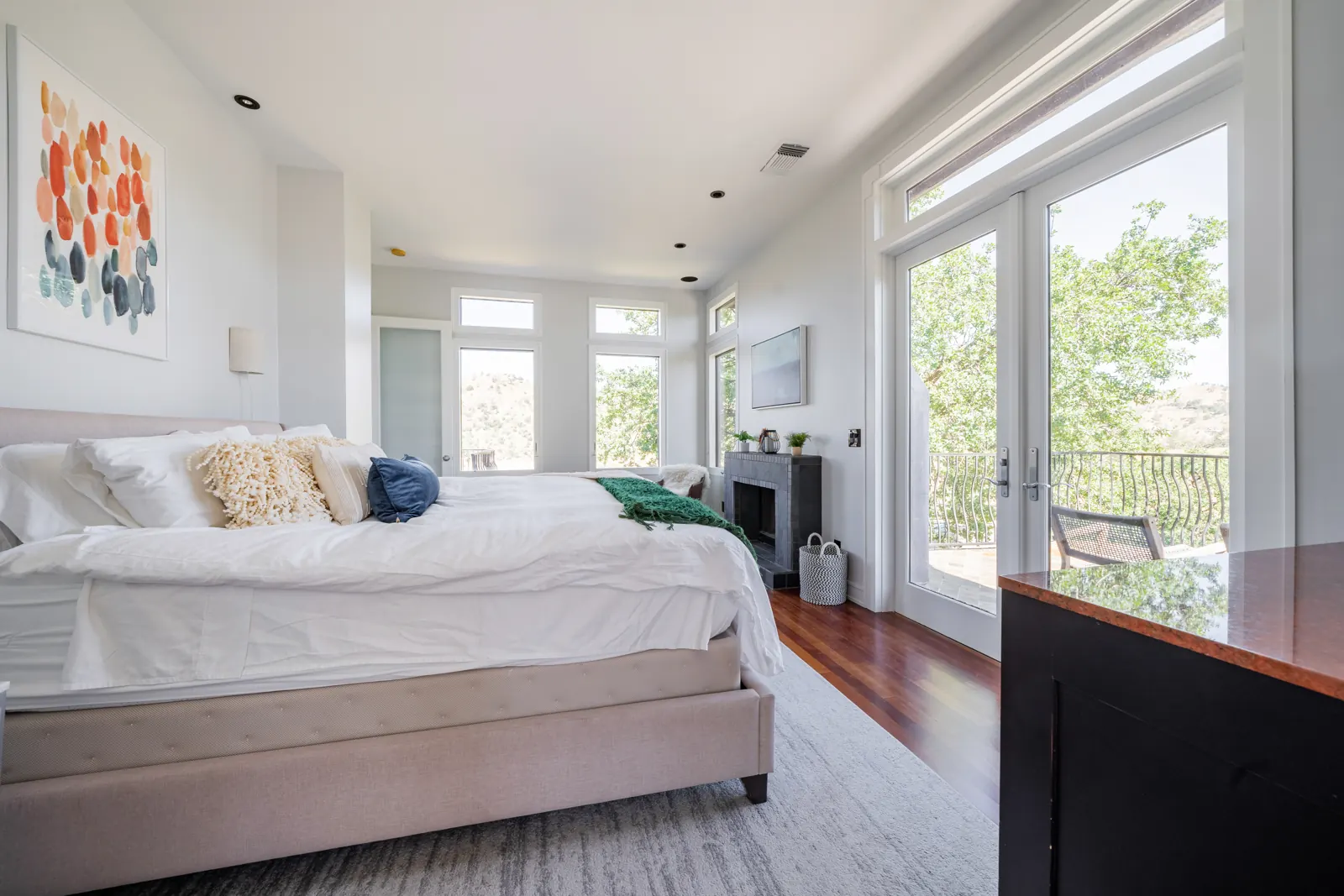 King bed in the primary suite with French doors open to the balcony and oak trees