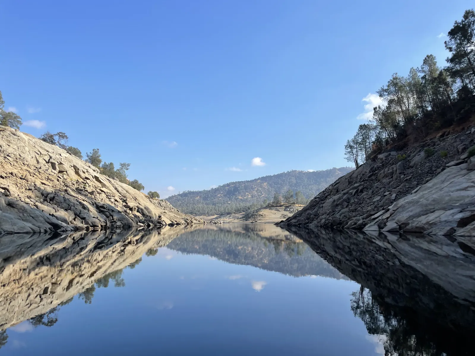 Still water reflecting granite banks and pine trees on a clear day